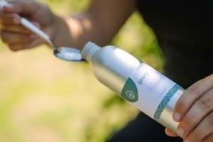 Georganics oil pulling mondwater wordt in een lepel gegoten, klaar voor gebruik in een natuurlijke buitenomgeving.